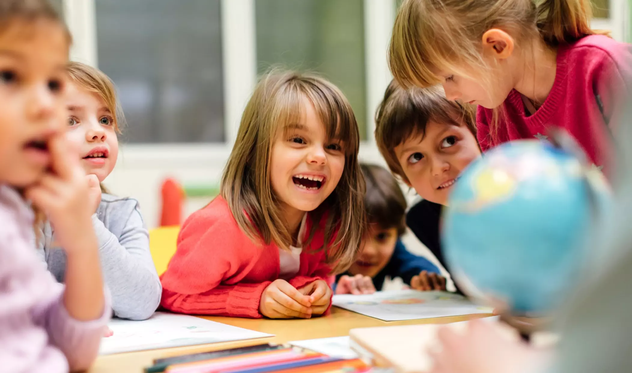 Vier Kinder im KiTa-Alter sitzen an einem Tisch. Ein Mädchen in der Mitte lacht herzlich.